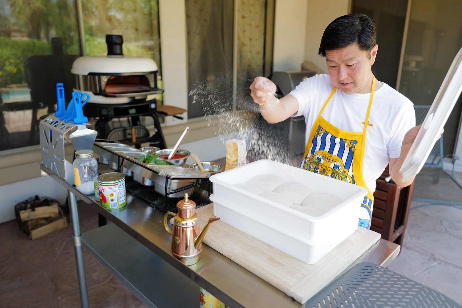 Alexander Yu's father dusting flour over pizza dough at a backyard oven in Arizona